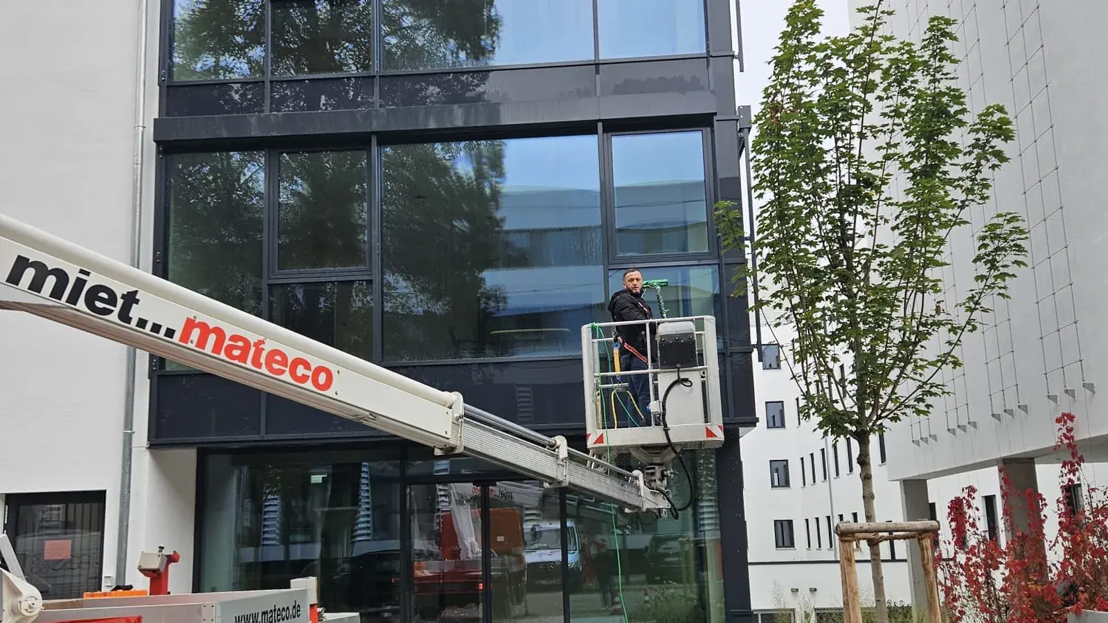 Mitarbeiter reinigt eine Glasfassade von der Hebebühne aus